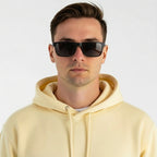Homem usando óculos de sol quadrados com armação preta e lentes escuras, look casual com moletom amarelo
