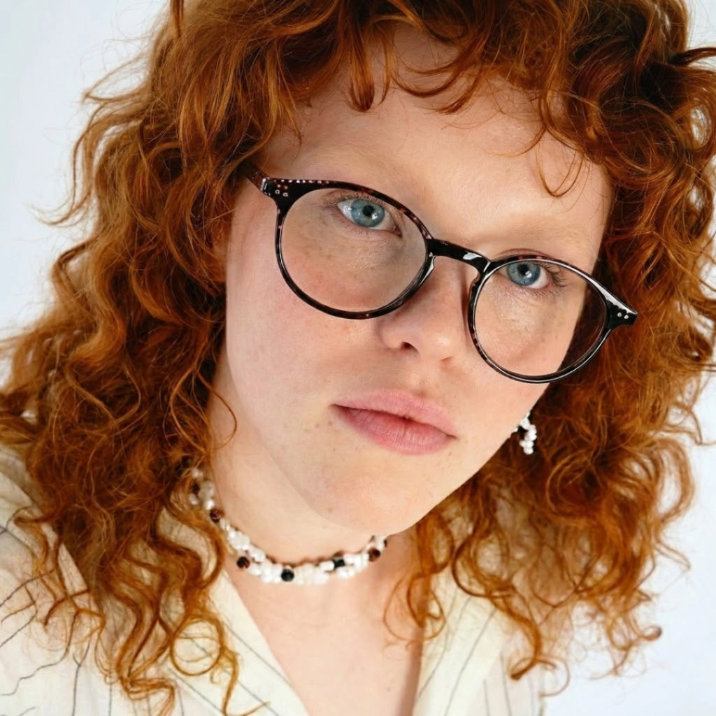 Mulher com óculos de grau redondos e cabelo cacheado vermelho, estilo moderno e elegante