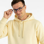 Homem usando óculos de grau azuis com hoodie amarelo claro, estilo moderno e confortável